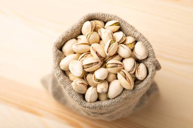 Small linen bag with pistachios on wooden table. Beautiful composition of pistachios, salted fresh nuts in bag