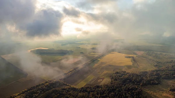 Flying high in the clouds over countryside. Aerial photo of clouds floating above countryside fields and forests, beautiful sunset from drone point of view