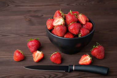 Bowl of strawberry and black knife on table. Juicy strawberry composition