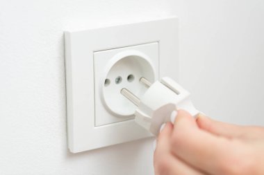 Inserting the electrical plug into outlet of the wall, white colour, close up. Consumption of electricity, modern technologies concept
