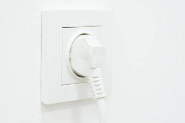 Electric plug in rosette on white wall, copy space. Consumption of electricity, household equipment, minimalism