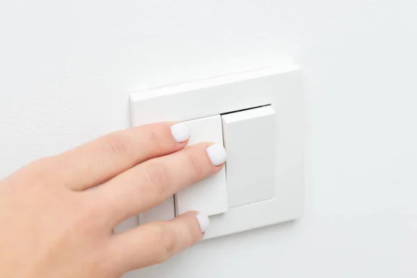 Turning on and off the light in the room with white walls. Close up picture of female hand on light switch