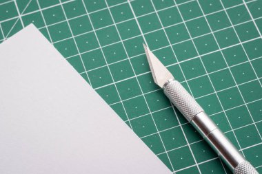Sharp scalpel near cut paper on cutting mat