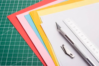 Profesyonel neşter, cetvel ve kesme hasırında farklı renkte kağıtlar üzerinde keskin bıçaklar.