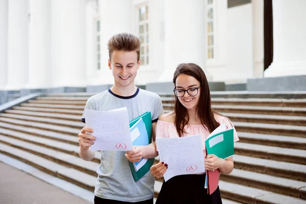 Happy cheerful students with test results near the university building boasting about high academic performance
