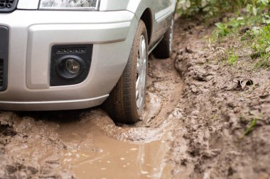 Modern hatchback car driving on bad dirt road with many puddles. Countryside road in terrible condition after Autumn rains