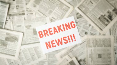 Wide picture of blurred newspapers on the table with the red inscription BREAKING NEWS in the middle on white paper