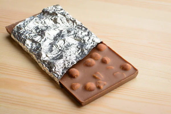 Bar of tasty chocolate with nuts covered with foil  lays on wooden table