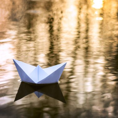 Small paper boat sailing down the river in Autumn at sunset. Concept of loneliness, abandonment, freedom