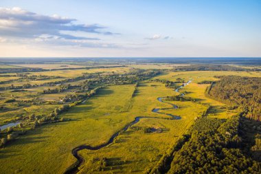 Valley of the river with small village on the background, aerial shot. Drone photo of small river near forest and village