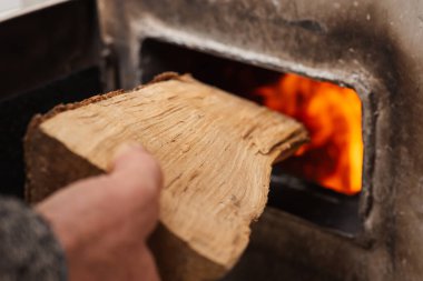 Man loads piece of firewood in the solid fuel boiler, flames on the background. Solid fuel and heating concept