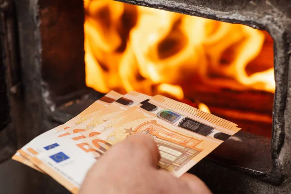 Man throwing euro money in the boiler with bright flames in it. Concept of high prices for heating the house, shortage of fuel and need to save money