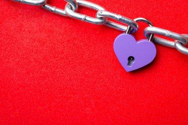 Small violet lock in shape of heart linked to the chain. Heart lock holding two pieces of chain like two people together. Concept of love, relationships