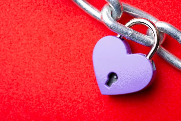 Close up of small violet lock in shape of heart linked to the chain. Concept of love, relationships, sweetheart