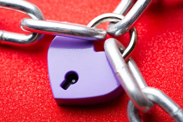 Small violet lock in shape of heart linked to the chain. Heart lock holding three pieces of chain. Concept of love