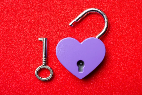 Close up of open lock in shape of heart. Little heart lock and key on red background