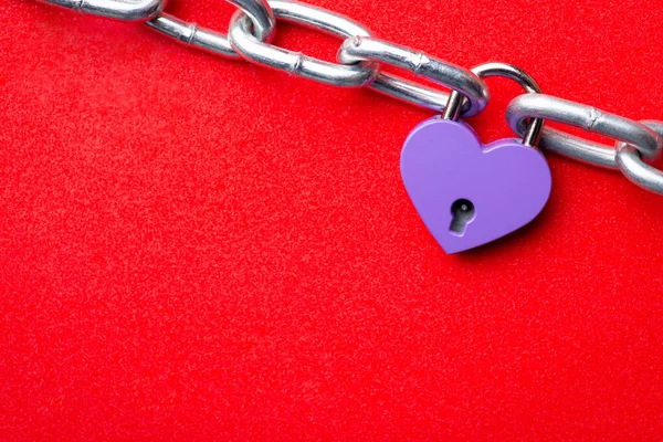 Small violet lock in shape of heart linked to the chain. Heart lock holding two pieces of chain like two people together. Concept of love, relationships