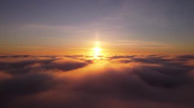 Bulutların üzerinde uçan drone videosu. Aşağıda eriyen hızlı bulutlar, arka planda çarpıcı bir günbatımı.