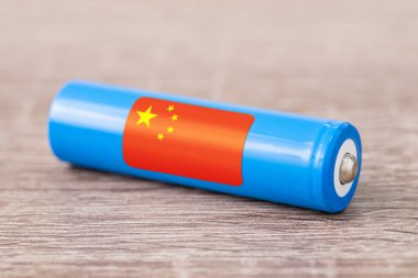 Close up shot of li-ion battery on wooden table with flag of China - world`s leading producer of rechargeable batteries. Concept of producing accumulators in China, origin of batteries