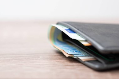 Grey wallet with euro money, close up on the wooden table, copy space on the left. Wealth, savings, purchases in Europe concept
