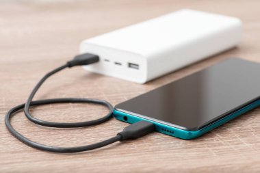 Charging modern smartphone from white powerbank. Power Bank and mobile phone on the table while charging