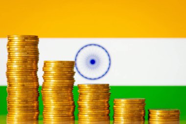 Flag of India with stacks of golden coins forming downcoming progression. Crisis in economy of India, negative process in finances of the country