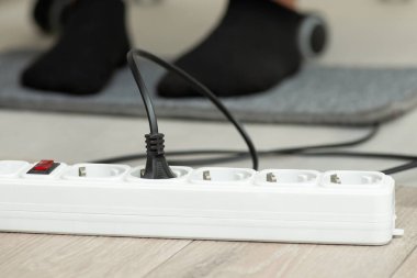 Close up of electric plug of warming mat turned on to the outlet. Warming foots while working on the computer