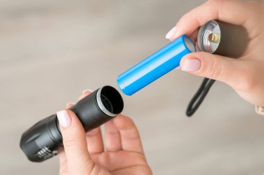 Black flashlight, female hands inserting blue 18650 battery in it, close up. Device for lightning, power for portable flashlight