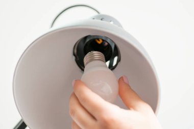 Close up shot of woman's hand changes a light bulb in grey lamp. Modern interior decor, office object for work, lightening the workplace