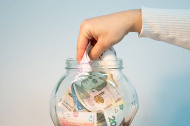 Kadın eli cam kavanozdan hryvnias biriktiriyor. Tasarruf zamanı, kavanozdaki Ukrayna hrivniaları