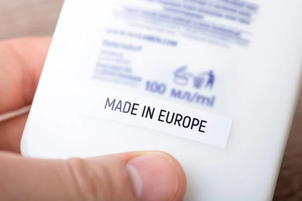 White tube of shampoo with Made in Europe inscription in hand of a man. Close up of inscription on product bottle, producing goods in EU concept