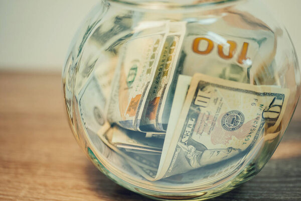 Close up of glass jar with dollar banknotes. Full of saved up money jar, toned photo