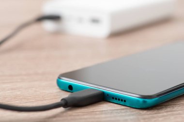 Telefonu USB kablosuyla şarj ediyor, arka planda da da elektrik bankası var. Şarj cihazları konsepti için güç bankası kullanılıyor