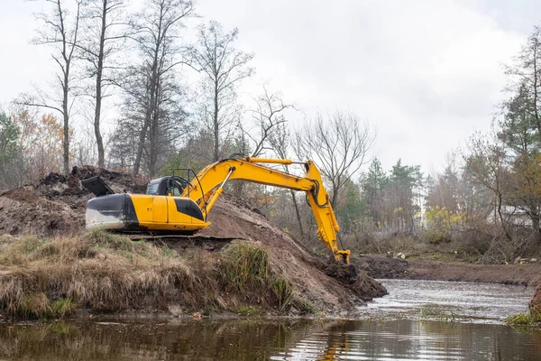 农村的大型工业挖掘机挖掘池塘 黄色挖掘机从人工池塘底部铲土 — 图库照片
