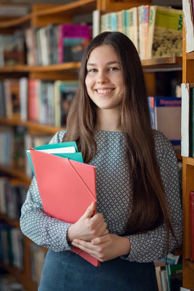 Happy smiling girl with folders in library. Diligent student girl eager to study and enlarge her knowledge