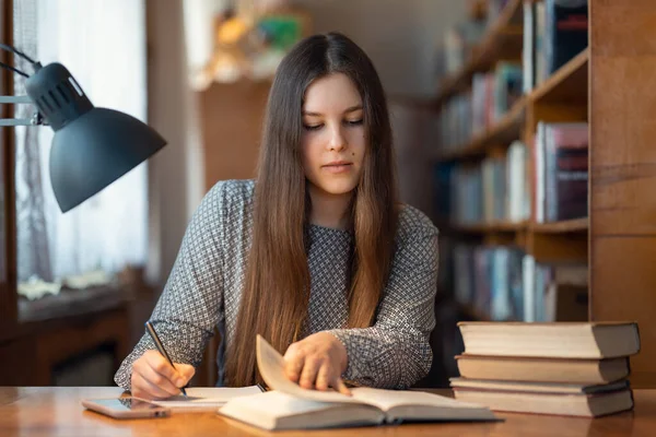 本を読み ノートを取り 彼女が読む最も重要な情報を書くスマートな若い女の子 大学図書館で受験勉強して机で働いている学生の女の子 — ストック写真