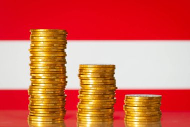 Three stacks of gold coins from highest to lowest against flag of Austria. Financial crisis in economy of Austria, recession