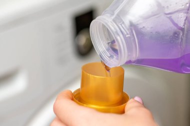 Şişenin kapağına sıvı menekşe jeli döken dişiyi kapatın. Ev işleri, çamaşır yıkama, ev işleri, çamaşır yıkama.