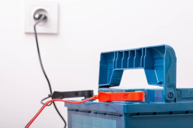 Araba akümülatörü bataryası beyaz duvarın yanındaki prizden şarj oluyor. Servis, bakım, şarj araba aküsü kavramı