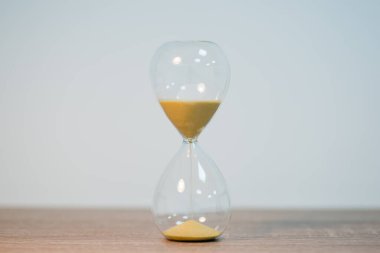 Beyaz arka plandaki ahşap masanın ortasındaki kum saatini kapat. Geçen zamanın sembolü, zaman aralıklarını ölçen, fotoğrafın iki tarafına boşluğu kopyalayan