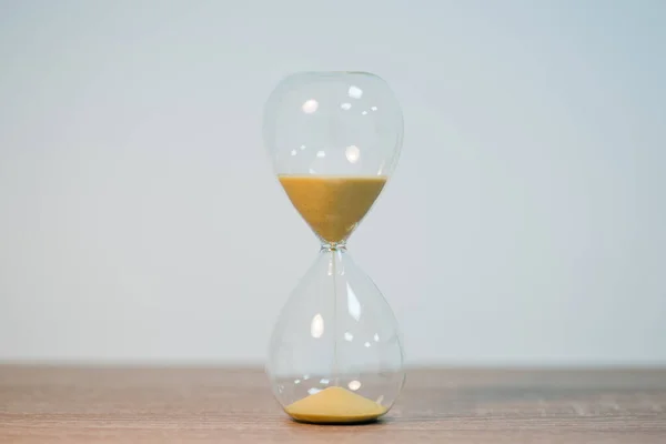 stock image Close up of sandglass in the middle of wooden table on the white background. Symbol of passing time, measuring the periods of time, copy space on two sides of photo