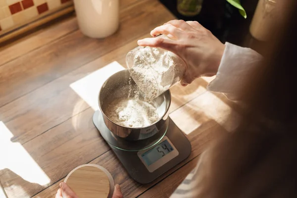 Measuring flour with electronic kitchen scales for cooking something. Girl pouring flour to the metal cup for precise measuring