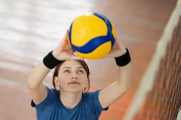 Genç kız vurmadan önce topu ağın üzerinden atıyor. Lisede voleybol antrenmanı yapan bir öğrenci, beden eğitimi dersi.