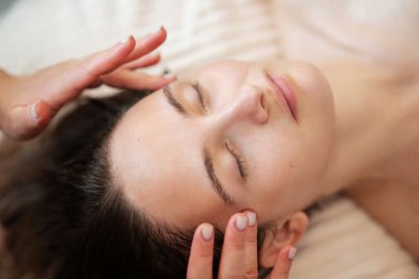 Yüz masajını tedavi ederken rahatlayan bir kız müşterinin yüzünü kapat. Masaj ile deriyi formda tutmak, kırışıklıkları önlemek, yüzdeki kan dolaşımını etkinleştirmek.