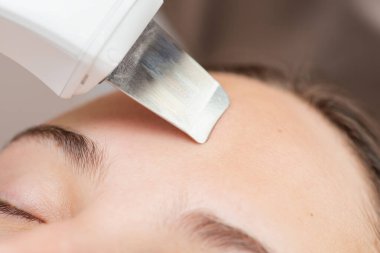 Genç bayan müşteriye ultrason cilt temizleme ve yüz soyma prosedürünü kapatın. Profesyonel elektronik temizlik cihazıyla kozmetoloji cilt temizliği
