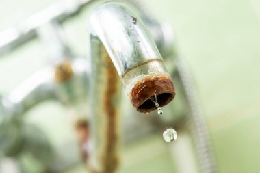 Eski musluktan damlayan, kireç ve pas kaplı makro su damlası. Su kıtlığı ve su tüketimi fikri