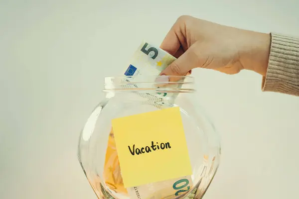 Saving money for vacation, toned photo. Person putting 5 euro banknote to the glass jar with inscription Vacation