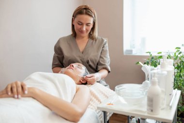 Kozmetik uzmanı, soğuk buharı ile temizlik yapan bir kızın yüzüne ince bir yapışkan film uyguluyor. Modern kozmetoloji teknikleri, sağlık ve cilt bakımı, profesyonel salon