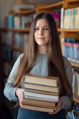 Kafası karışmış kitaplarla dolu esmer bir kız. Çalışma zamanı kavramı, zor görevler, çok iş, kütüphanede bilgi arama