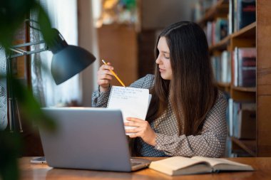 Esmer kız öğrenci online ders alıyor, öğretmenine ve sınıf arkadaşlarına bazı yazılı bilgiler gösteriyor. Bilgi, eğitim, modern teknoloji ve öğrenci hayatı kavramı